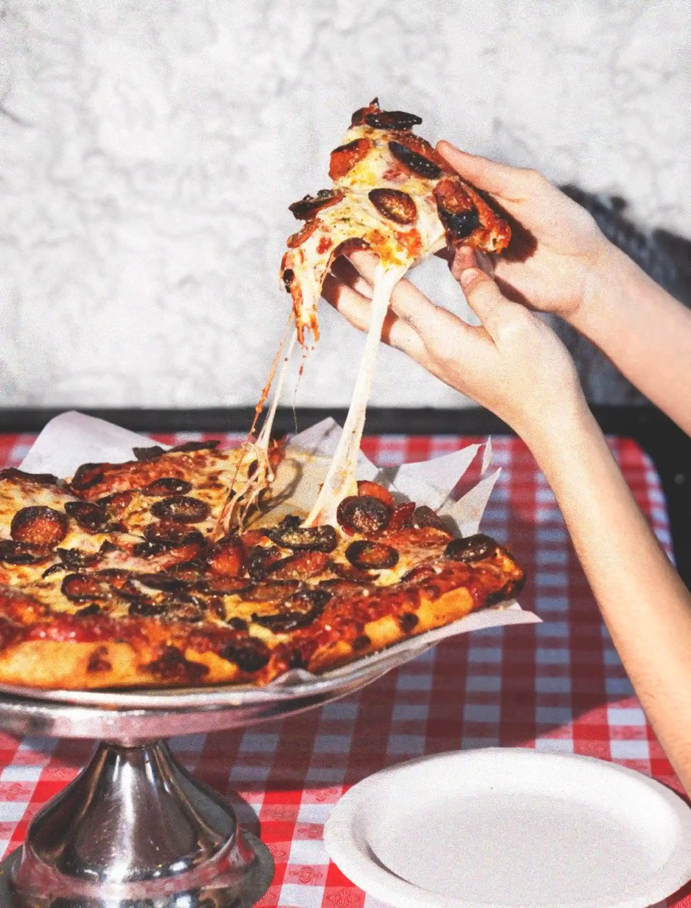 A person holding a slice of pepperoni and black olive pizza